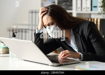 Triste femme de direction avec masque de protection, qui a trop lu les mauvaises nouvelles sur l'ordinateur portable au bureau la nuit Banque D'Images