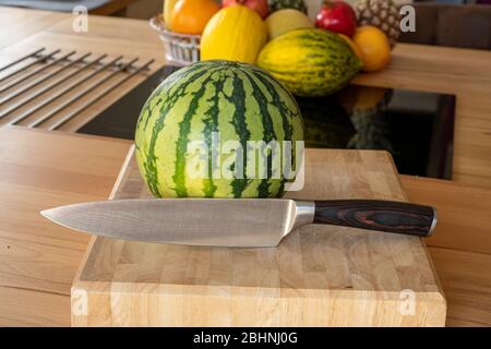 Vue rapprochée sur le melon d'eau douce et un couteau de cuisine de damas debout sur une île de cuisine dans une cuisine domestique avec d'autres variétés de fruits dans le TH Banque D'Images