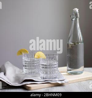 Limonade au citron avec estragon en bouteille transparente sur table sur fond de mur gris. Deux verres ondulés avec tranches de citron. Serviette grise et