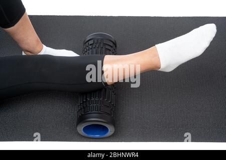 Une femme d'âge moyen sur un rouleau myofascial fait un massage de jambe de shin sur un fond blanc. Banque D'Images