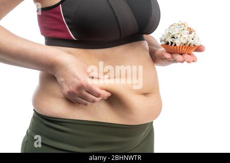 Femme d'âge moyen, obèse et peau venteuse du ventre, avec un cupcake sur un doson sur fond blanc, gros plan. Banque D'Images