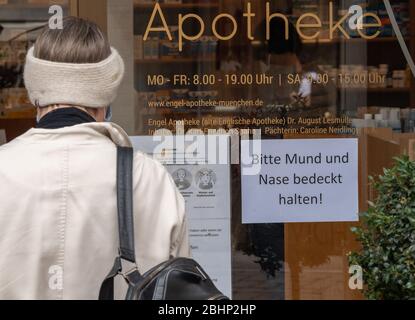 Munich, Allemagne. 27 avril 2020. Une femme se tient devant une pharmacie avec un panneau à l'entrée disant: "Gardez votre bouche et votre nez couverts! A partir de cette semaine, les magasins de 800 mètres carrés de surface de vente en Bavière pourront rouvrir dans certaines conditions. Toutefois, une obligation stricte de protection de la bouche et du nez s'applique dans les magasins et les transports publics. Crédit: Peter Knelove/dpa/Alay Live News Banque D'Images