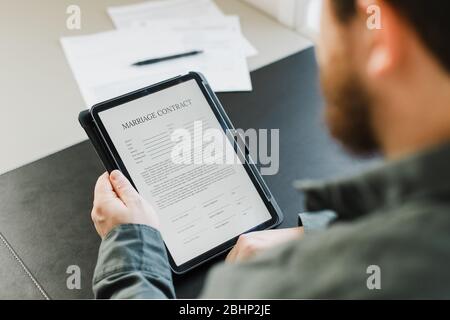 Gros plan homme lisant le contrat de mariage sur tablette au bureau. Banque D'Images