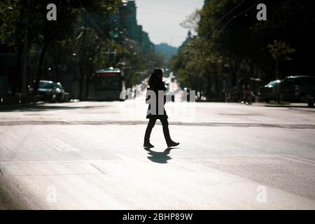 Bucarest, Roumanie - 22 avril 2020: Silhouette d'une femme traversant une route dans le centre de Bucarest pendant le verrouillage du covid-19 au crépuscule. Banque D'Images