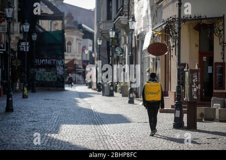 Bucarest, Roumanie - 22 avril 2020: Homme transportant un sac à dos Glovo livraison dans les rues vides de la vieille ville de Bucarest pendant le verrouillage covid-19. Banque D'Images