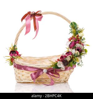 Panier rond en osier avec compositions fleuries de Pâques sur la poignée du panier. Décoration avec roses sombres et fleurs blanches. Isolé Banque D'Images