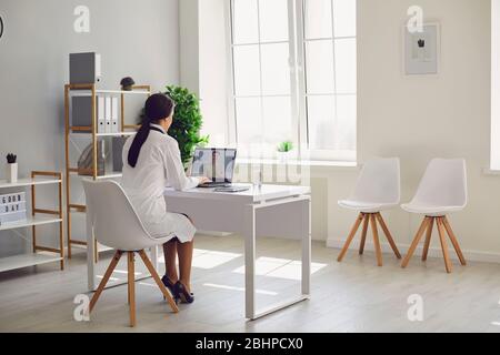 Médecin en ligne. Le médecin travaille à parler avec le patient en utilisant la chaussure de baste tout en étant assis au bureau dans le bureau de la clinique de vue arrière. Banque D'Images