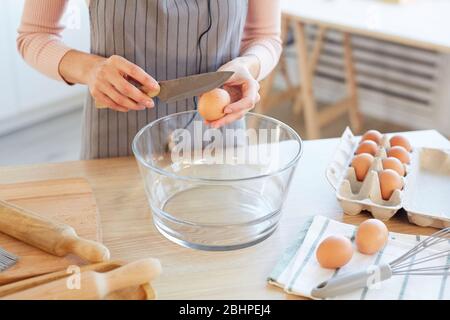 Jeune femme méconnaissable qui craque l'oeuf dans un bol en verre pour pâte de boulangerie, tir horizontal à angle élevé Banque D'Images