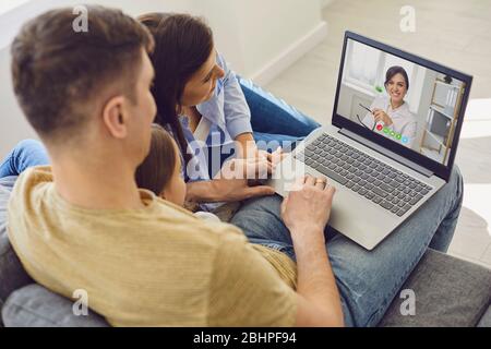 Consultation médicale en ligne pour les patients de la famille. Médecin femme appel vidéo utilisant un ordinateur portable parle avec la famille assis sur le canapé à la maison. Banque D'Images