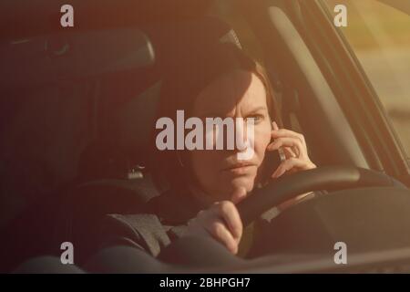 Femme d'affaires parlant sur le téléphone mobile dans la voiture tout en conduisant au travail, foyer sélectif Banque D'Images