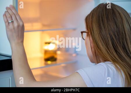 Femme se poste dans un réfrigérateur et voit seulement un pot de cornichons dans le réfrigérateur. Femme inspectant son réfrigérateur presque vide à la maison pendant l'auto-isolation. Banque D'Images