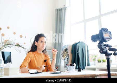 Blogueur de beauté assis seul dans sa chambre expliquant quelque chose aux spectateurs, prise horizontale Banque D'Images