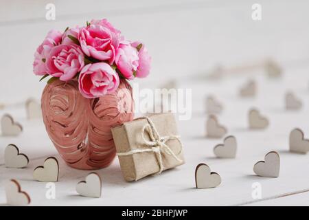 Fond vintage avec coeurs, boîte cadeau et bouquet de roses roses roses dans un vase sur panneau blanc en bois Banque D'Images