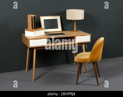 Bureau ancien en bois vintage avec lampe de table rétro, cadre photo et fauteuil dans un intérieur de chambre au décor gris Banque D'Images