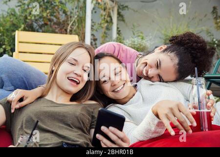 Trois femmes se détendent ensemble, riant et regardant un téléphone mobile. Banque D'Images