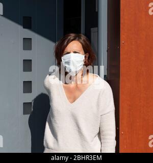Femme portant un masque à la maison, devant la porte Banque D'Images