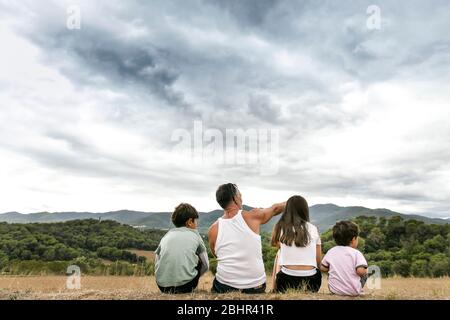 Vue arrière de la famille avec deux enfants assis dans le paysage, montagnes au loin. Banque D'Images