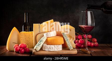 Panorama du fromage, mdivers fromages avec raisins et vin verseur, vue latérale sur un fond sombre avec un endroit pour le texte Banque D'Images