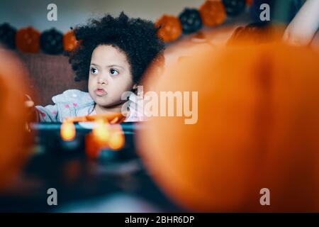Une petite fille à une table avec des citrouilles au premier plan. Banque D'Images