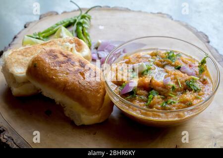 célèbre cuisine indienne de rue pav bhaji décoré sur une assiette en bois sur fond gris et garni d'oignon cru citron coriandre et de piments verts Banque D'Images