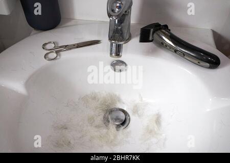 ciseaux à poils gris et tondeuse à cheveux bon marché dans un évier en raison de l'homme d'âge moyen qui coupe ses propres cheveux en raison de la pandémie de covid-19 auto-isolée Banque D'Images
