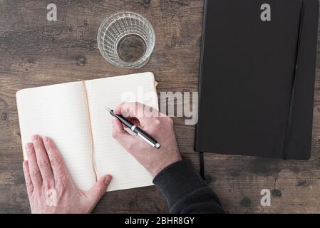 vue de dessus de la personne au bureau en bois prenant des notes dans le journal ou le journal Banque D'Images