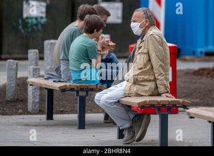 Hambourg, Allemagne. 27 avril 2020. Un homme porte un masque de protection de la bouche du nez tout en étant assis sur un banc à côté des jeunes qui mangent de la glace. Crédit: Axel Heimken/dpa/Alay Live News Banque D'Images