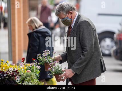 Hambourg, Allemagne. 27 avril 2020. Un homme porte un masque de protection de la bouche du nez tout en tenant des pots de fleurs dans sa main devant un fleuriste. Crédit: Axel Heimken/dpa/Alay Live News Banque D'Images