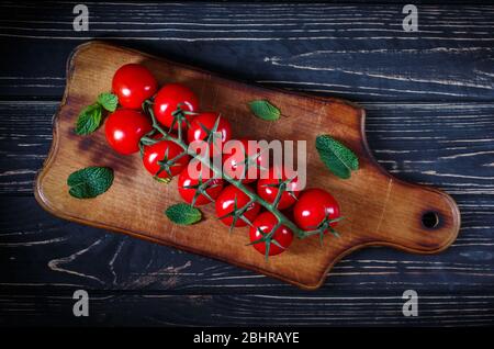 Composition de plat avec tomates entières fraîches sur une branche. Tomates et feuilles de menthe sur une table en bois. Banque D'Images