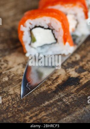 Des petits pains à sushis avec légumes, fromage et saumon sont posés sur une lame de couteau. Banque D'Images