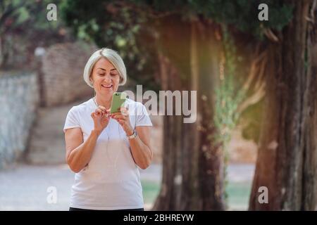 Femme senior en parc avec smartphone et écouteurs Banque D'Images