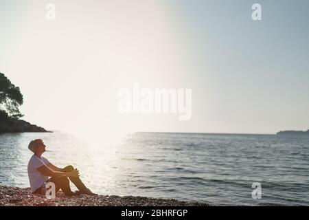 Femme mûre assise après le jogging sur la plage au coucher du soleil. Course en soirée Banque D'Images