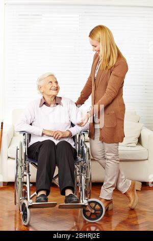 Une femme âgée souriante en fauteuil roulant reçoit une visite à domicile du service de soins infirmiers Banque D'Images