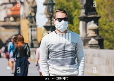 Jeune homme avec lunettes de soleil et masque en tissu cousu photographié sur le pont Charles à Prague, en République tchèque. Arrière-plan flou. Voyager, tourisme pendant coronavirus. COVID-19. Banque D'Images
