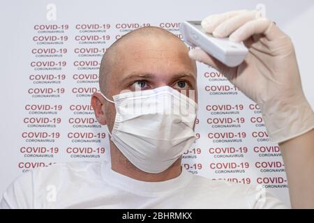 Le portrait d'un malade portant un masque médical et des gants est de vérifier la température à l'aide d'un thermomètre infrarouge. COVID-19 texte coronavirus à blanc backgrou Banque D'Images