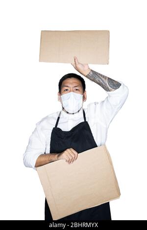Barbu asiatique homme serveur, chef vêtu d'un tablier noir avec masque médical tient carton en blanc. Le concept de protestation, attention, re Banque D'Images