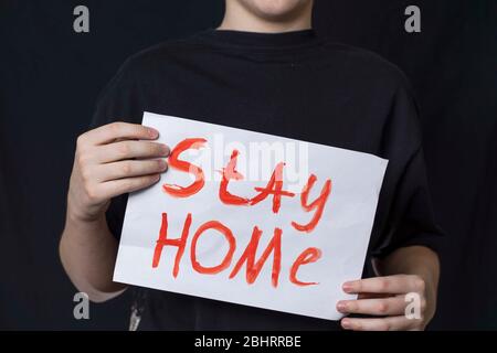 Un adolescent dans un T-shirt noir se tient avec l'inscription rester à la maison. Tenant une affiche en lettres rouges rester à la maison. Quarantaine, coronavirus covid19 Banque D'Images