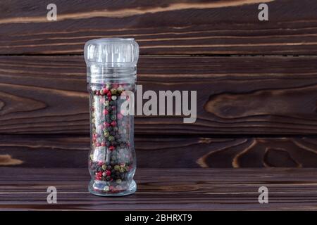 Pois de poivre colorés dans un bocal en verre sur fond de panneaux en bois brun foncé, graines multicolores de poivre épicé, rouge chaud et poivre noir dans la bouteille. Banque D'Images