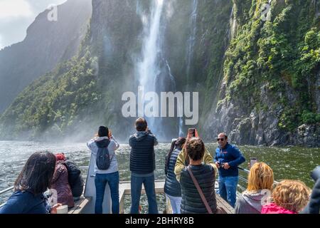 Milford Sound, Nouvelle-Zélande. Les touristes photographiant les chutes Stirling depuis le pont d'un bateau de croisière, Milford Sound, Fiordland National Park, Nouvelle-Zélande Banque D'Images