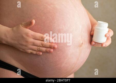 La femme enceinte frotte l'huile des marques de stretch dans son ventre Banque D'Images