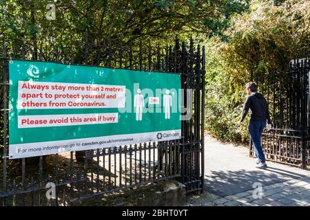 Un homme entre dans Waterlow Park, une grande bannière près des portes conseillant dans la distanciation sociale pendant le verrouillage pandémique du coronavirus, Londres, Royaume-Uni Banque D'Images