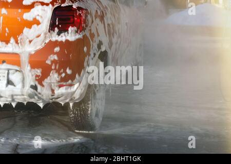 La voiture est en cours de nettoyage avec des suds de savon au lavage de voiture en libre-service. Tramage blanc sur auto. Des projections d'eau autour de la voiture et de l'eau savonneuse s'écoule. Banque D'Images