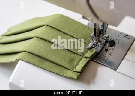 Vue rapprochée sur un masque en tissu réutilisable fait maison dans un tissu en coton vert cousu sur une machine à coudre. Banque D'Images
