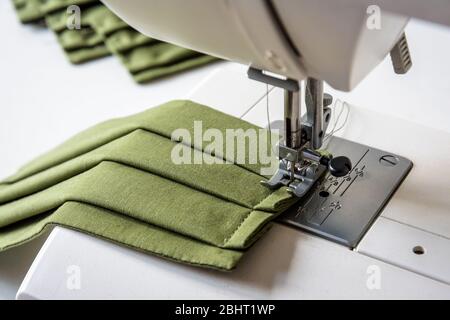 Vue rapprochée sur un masque en tissu réutilisable fait maison dans un tissu en coton vert cousu sur une machine à coudre. Banque D'Images