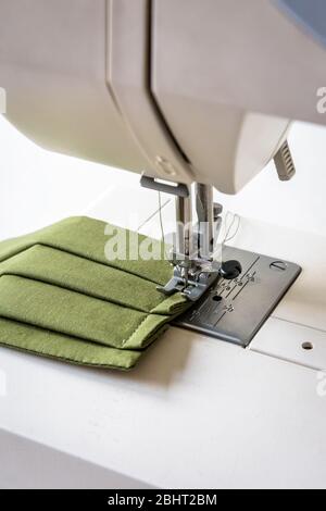 Vue rapprochée sur un masque en tissu réutilisable fait maison dans un tissu en coton vert cousu sur une machine à coudre. Banque D'Images