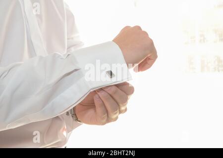 Gros plan du bras d'un homme qui met un beau boutons de manchette sur le brassard de sa chemise blanche. Banque D'Images