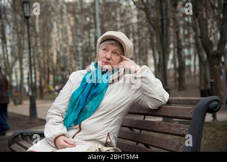 Une vieille femme habillée avec élégance est assise sur un banc dans une ruelle. Banque D'Images