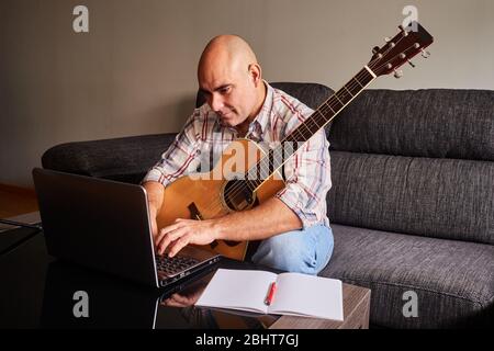 Concept: Apprendre en ligne à la maison. Homme adulte d'âge moyen. Bald homme avec chemise de secours dans son salon. Jouer de la guitare. Didacticiel Internet. Banque D'Images