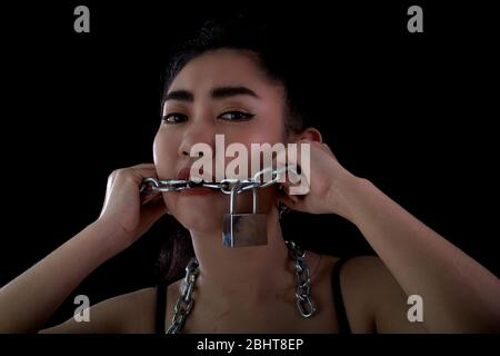 Portrait jeune femme d'Asie couverte de bouche par une chaîne en acier et de verrouiller pour lui interdire la voix libre sur fond noir, Arrêter ou cesser de parler Banque D'Images