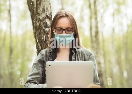 Indépendant pendant la quarantaine dans la nature. Femme en masque travaille sur un ordinateur portable en forêt. Concept de travail à distance Banque D'Images